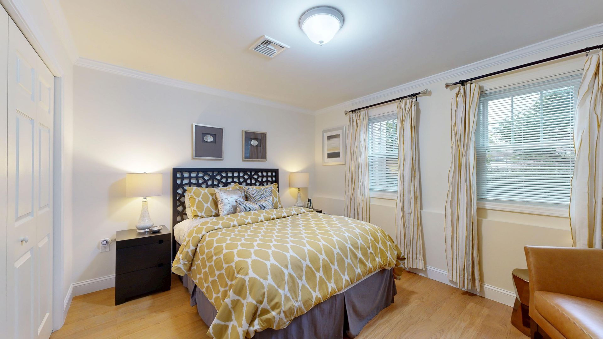Bright bedroom with yellow patterned bedding, two windows, and a bedside lamp.
