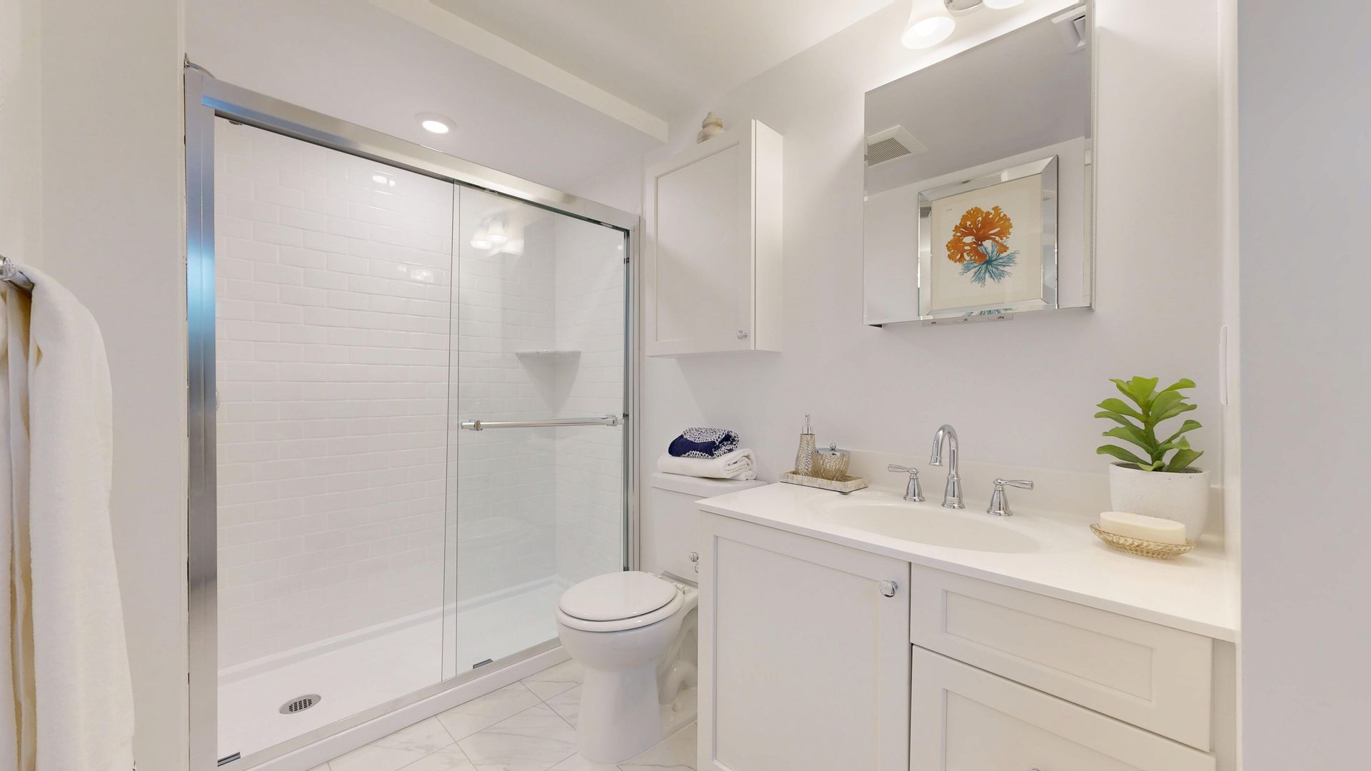Bright white bathroom with glass shower, vanity, mirror, and a small stool.