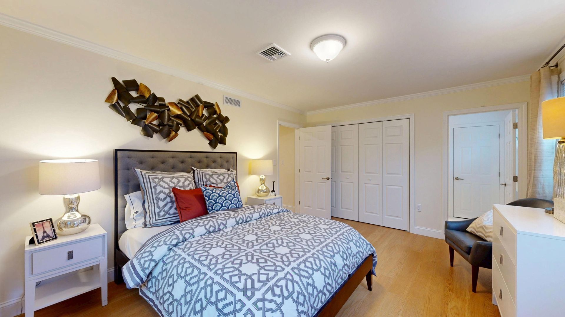 Bright bedroom with a bed, nightstands, white closets, and warm lighting