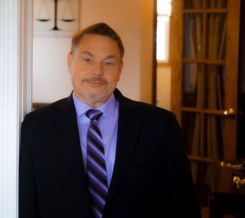 Ty Mahffey in a dark suit and purple tie standing indoors by a doorway, facing the camera.