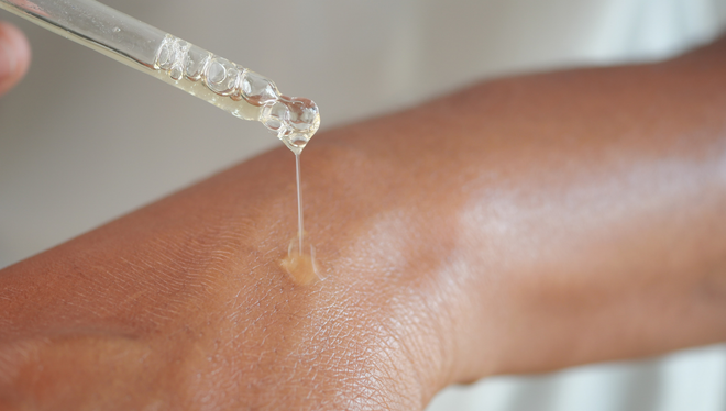 Eye dropper releasing liquid onto skin in a close-up