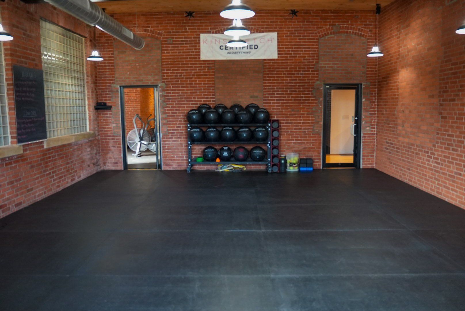 Gym interior with black floor, brick walls, fitness equipment, and overhead lighting.
