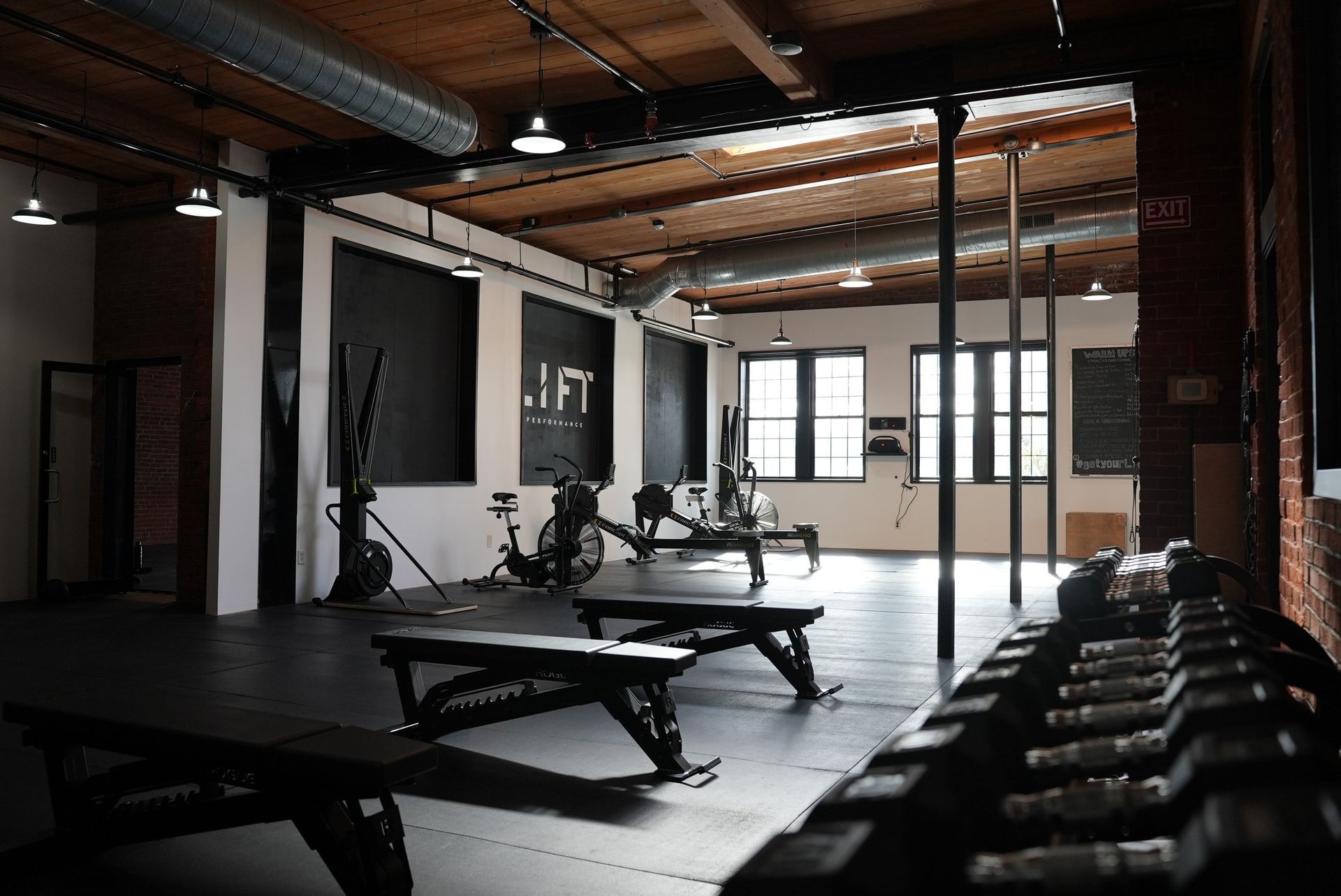 Gym interior with exercise equipment, including weights, benches, and rowing machines, in a large open space.