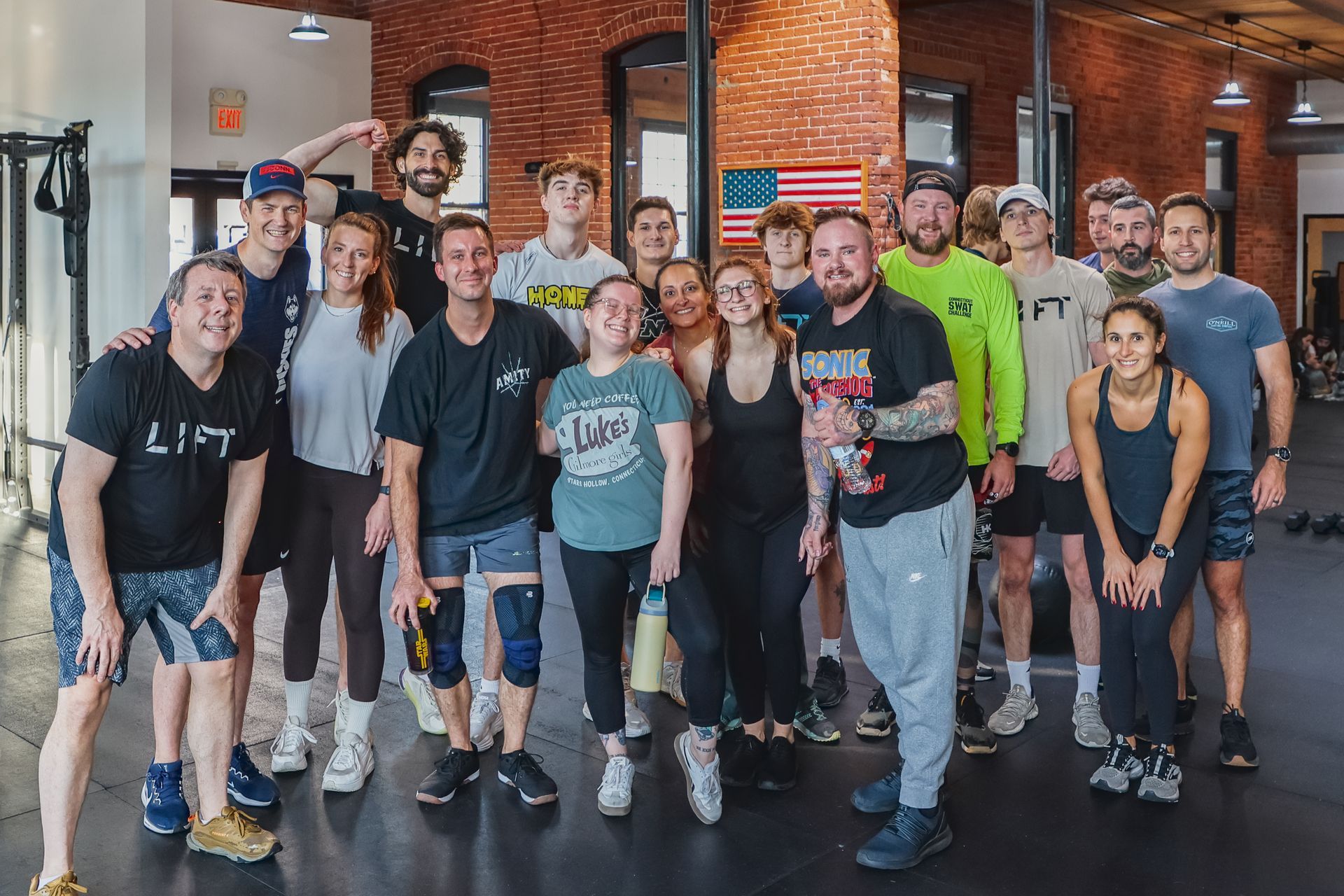 Group of people smiling in a gym. An American flag is visible on the brick wall.