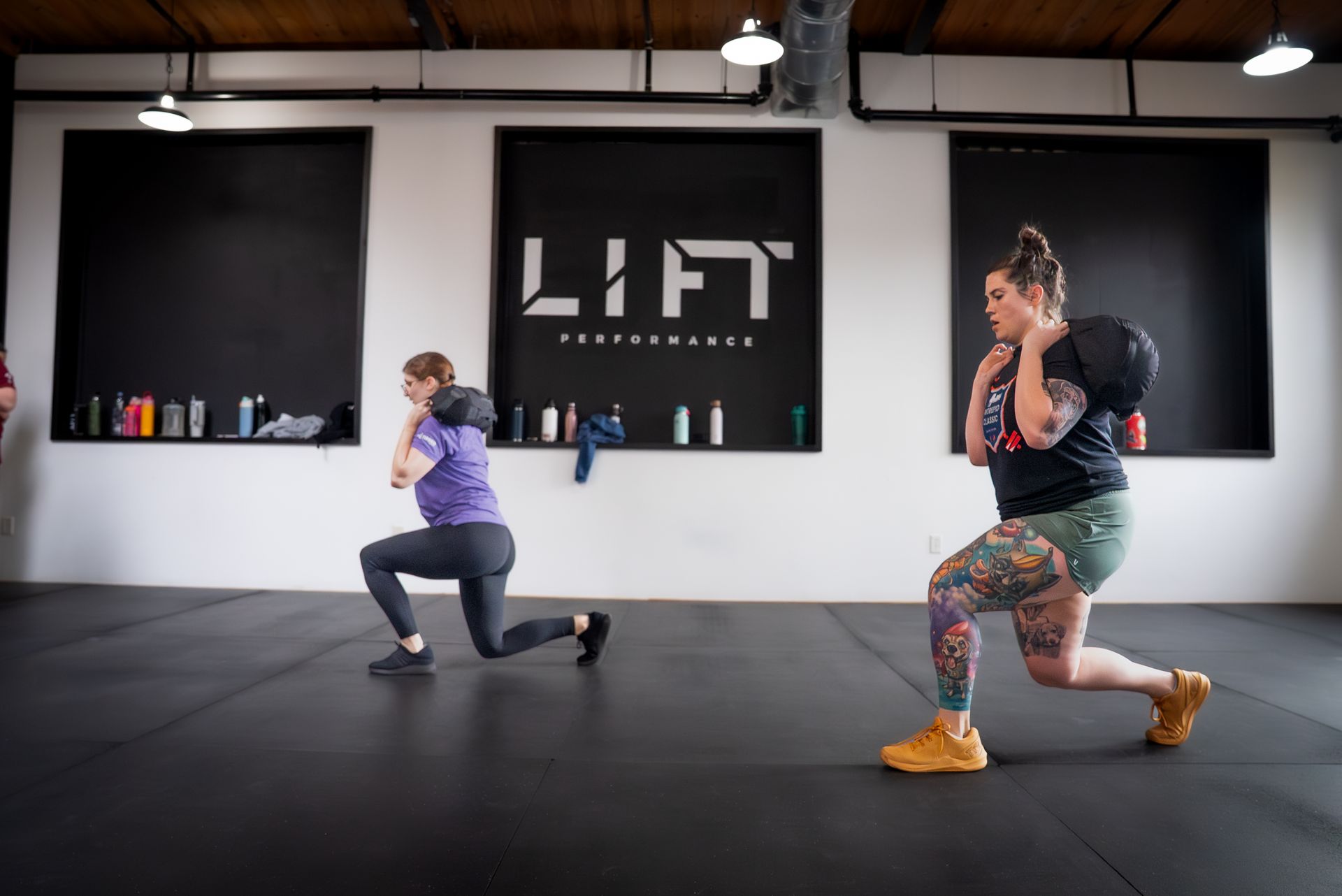 Two people doing lunges in a gym studio with LIFT sign on the wall