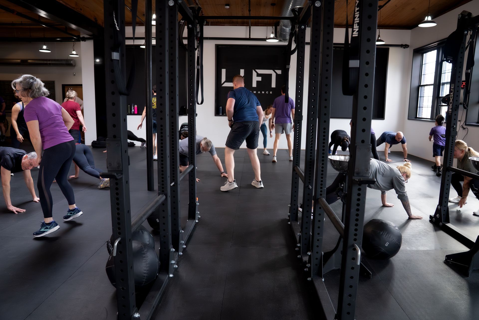 People exercising in a CrossFit gym with pull-up rigs, kettlebells, and large windows