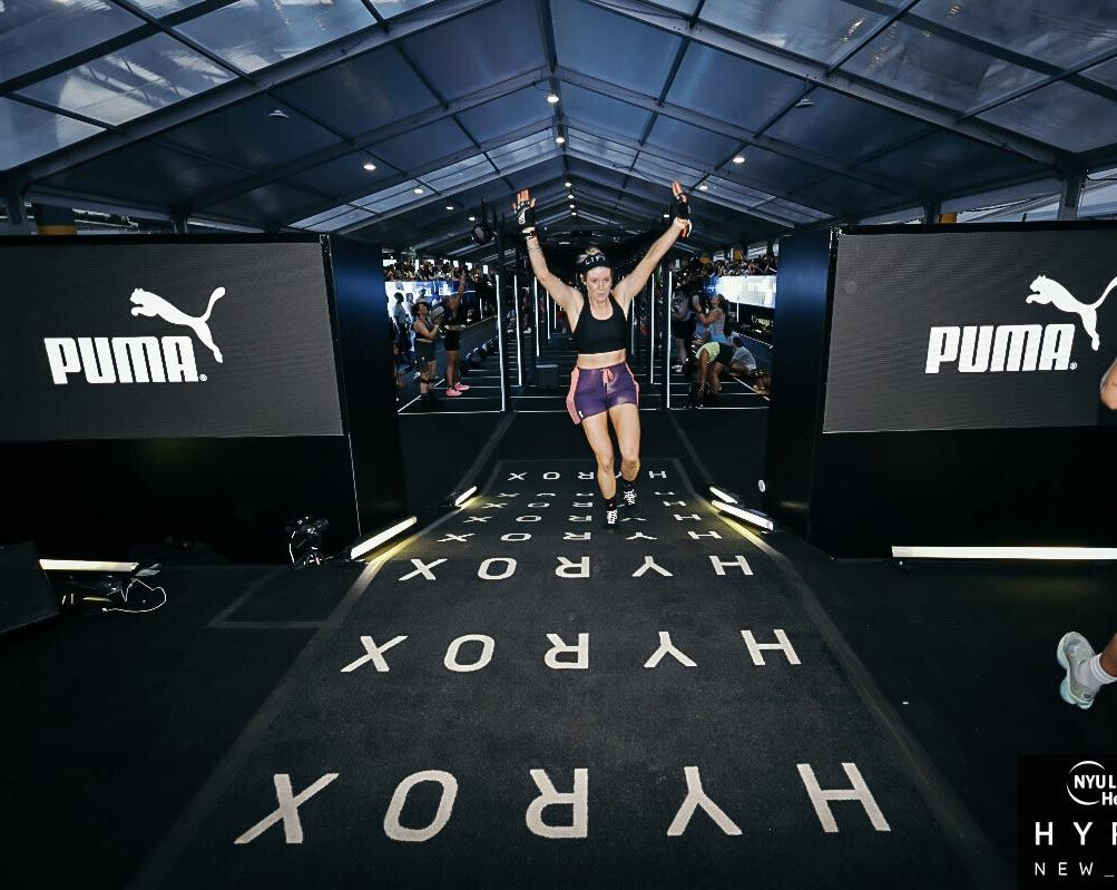 Athlete crossing a finish line at a HYROX event between large PUMA banners, arms raised in victory