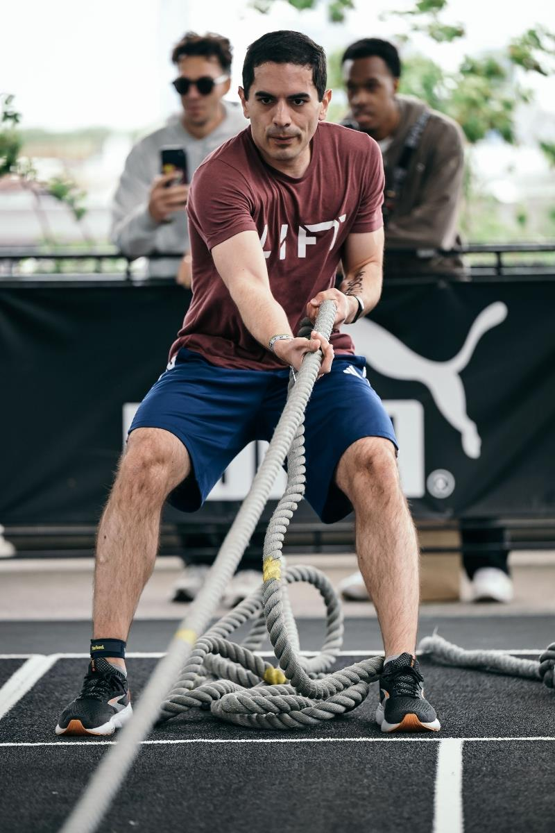 Man pulling heavy battle ropes on an outdoor track, with two people watching behind him.
