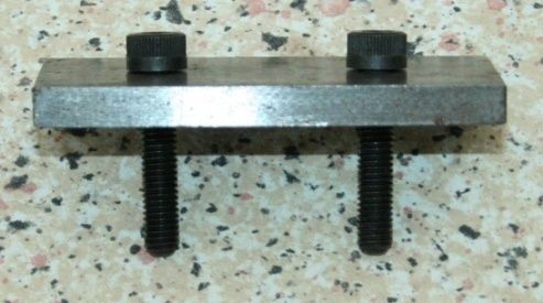 Metal clamp with two black bolts, on a speckled surface.