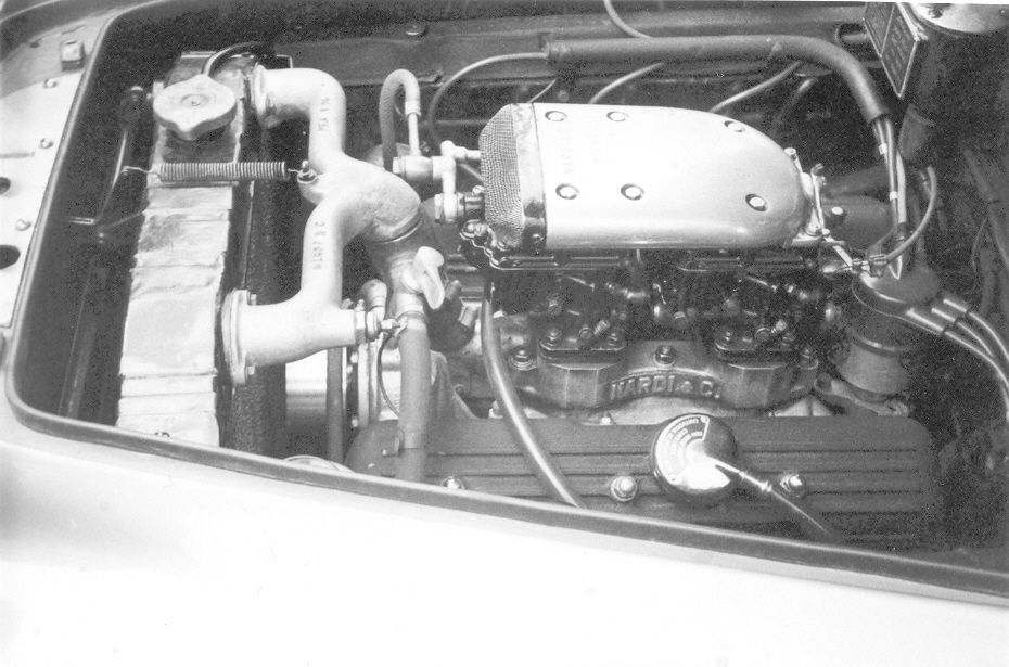 Engine of a vintage car, viewed from above. Silver metal components dominate the scene, including intake and cooling systems.