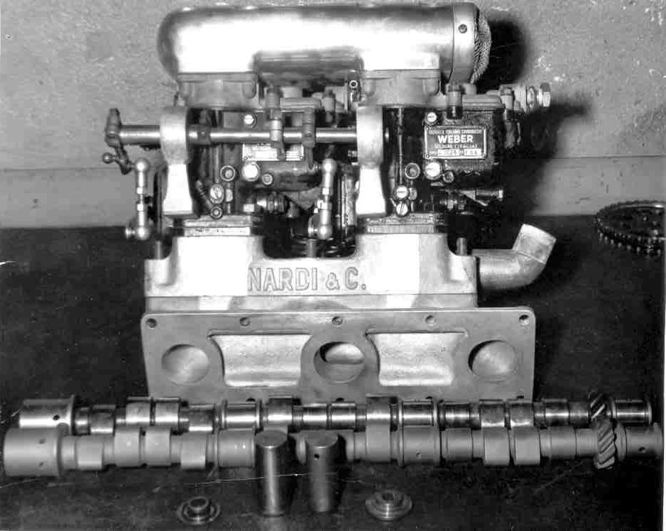 Engine block with parts displayed, including a camshaft, on a table.
