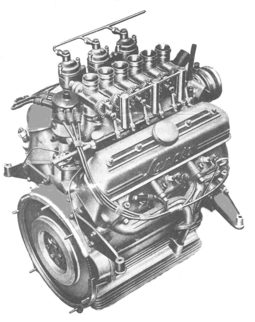 Silver automobile engine with multiple carburetors and mechanical components.