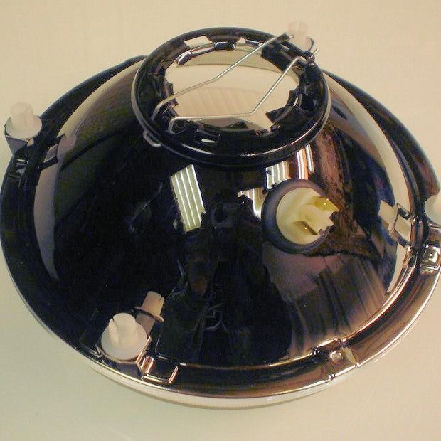 Black automotive headlight, chrome trim, white bulbs visible, reflective surface.