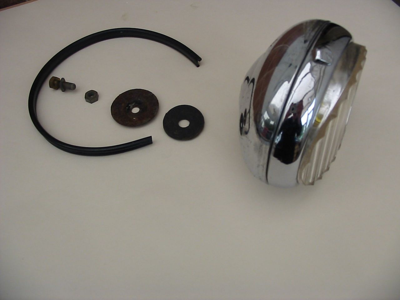 Chrome headlight assembly with parts, including a gasket, on a white surface.