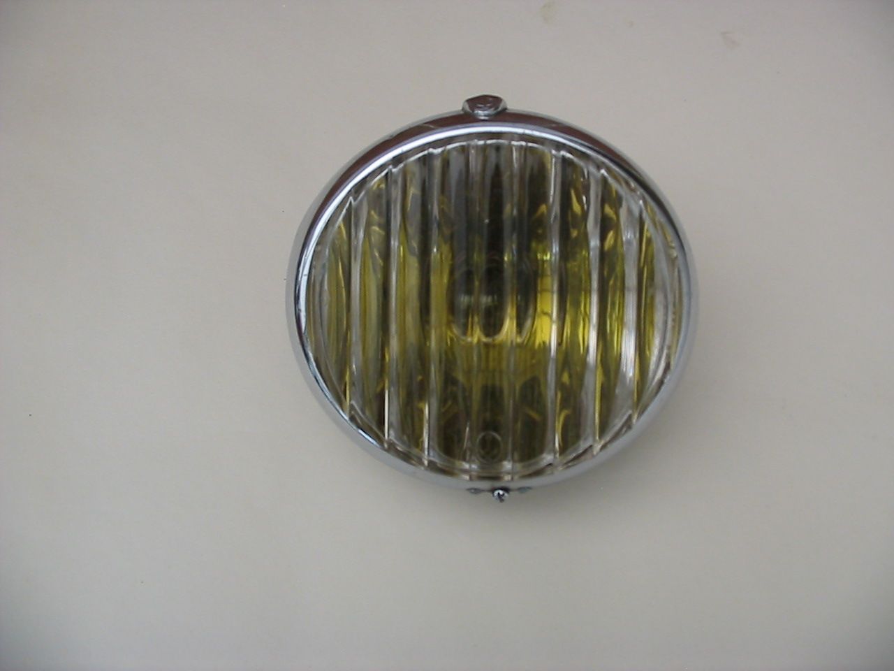 Chrome-ringed, round car headlight with yellow-tinted ribbed glass against a cream background.