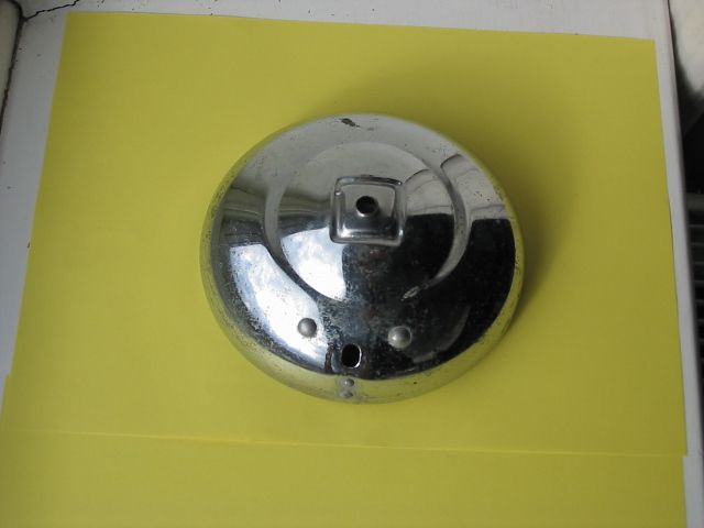 Shiny, round, chrome metal object with a square hole, resting on a yellow surface.