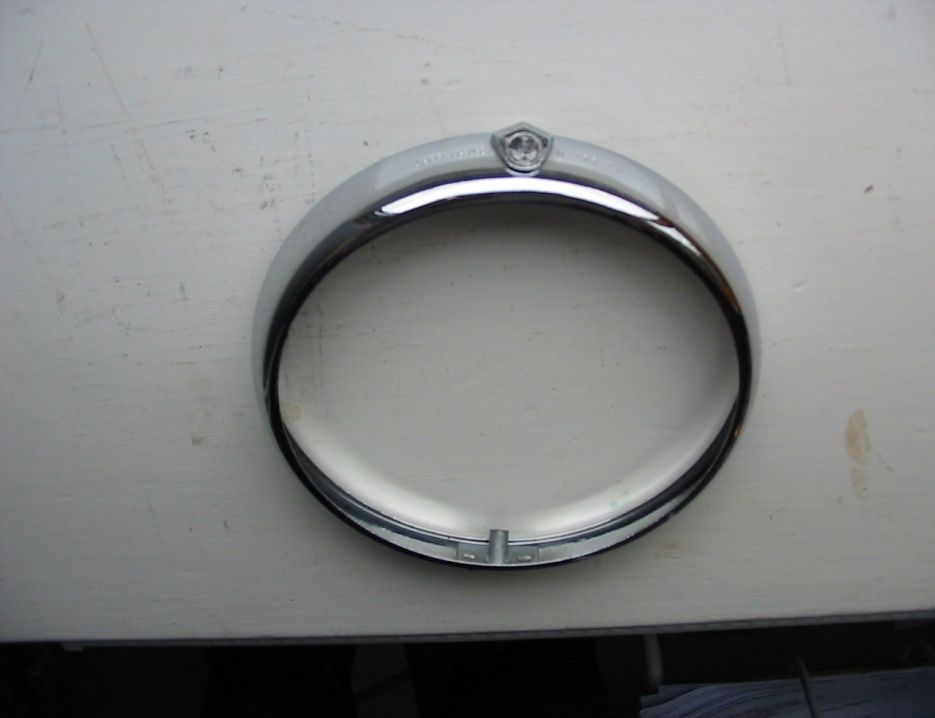 Chrome-plated headlight bezel with emblem, circular shape, on a white surface.