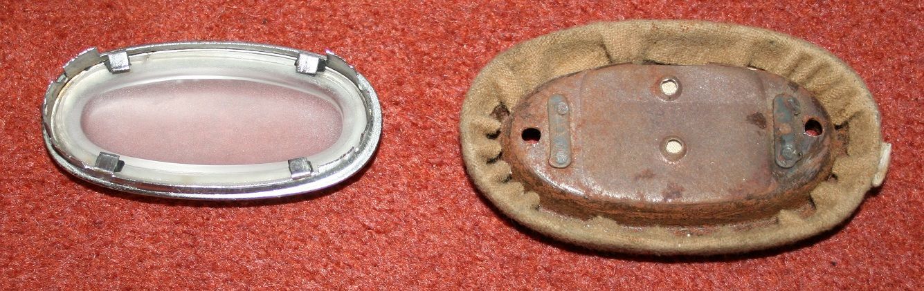 Two oval objects on a red surface: a clear, framed lens and a corroded back panel with padding.