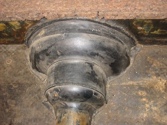 Black rubber plumbing boot sealed around a pipe, set in a rusty metal floor.