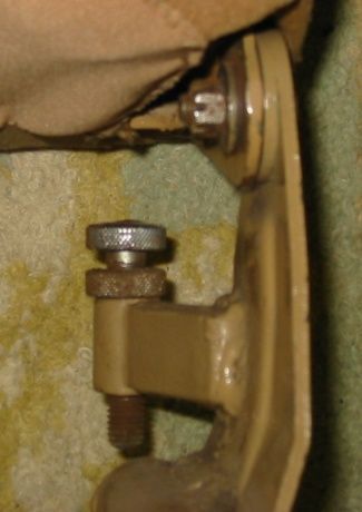Close-up of a tan metal bracket with bolts and a threaded knob, attaching to a tan fabric object.