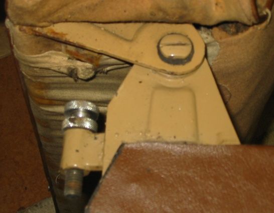 Tan metal bracket with a screw and a silver knob, connected to tan and brown surfaces.