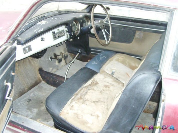 Interior of an old, red coupe, showing weathered black and tan seats, steering wheel, and dashboard.