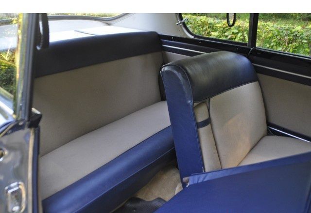 Interior car view, showing blue and tan upholstery on front and back seats, near a window.