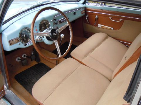Tan interior of a classic car with wooden accents, pale blue dashboard and steering wheel, beige seats.