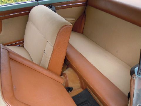 Tan and brown vintage car interior; two rows of seats.