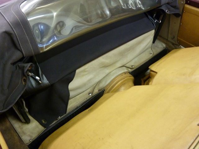 Interior of a convertible car, showing a black tonneau cover and tan upholstery.