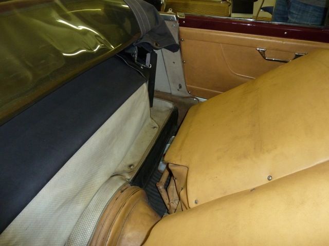 Interior view of a convertible car, showing tan seats, black trim, and burgundy door.