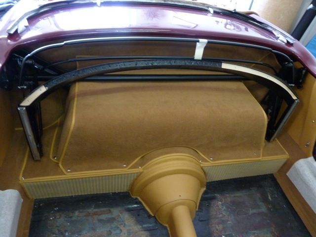 Interior of a vintage car with tan carpet and a dark-colored framework, viewed from the rear.
