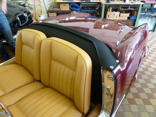 Tan leather seats in a maroon vintage convertible with a black top; indoors.