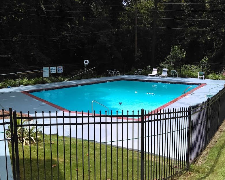 Outdoor swimming pool with bright blue water, surrounded by a black metal fence and trees