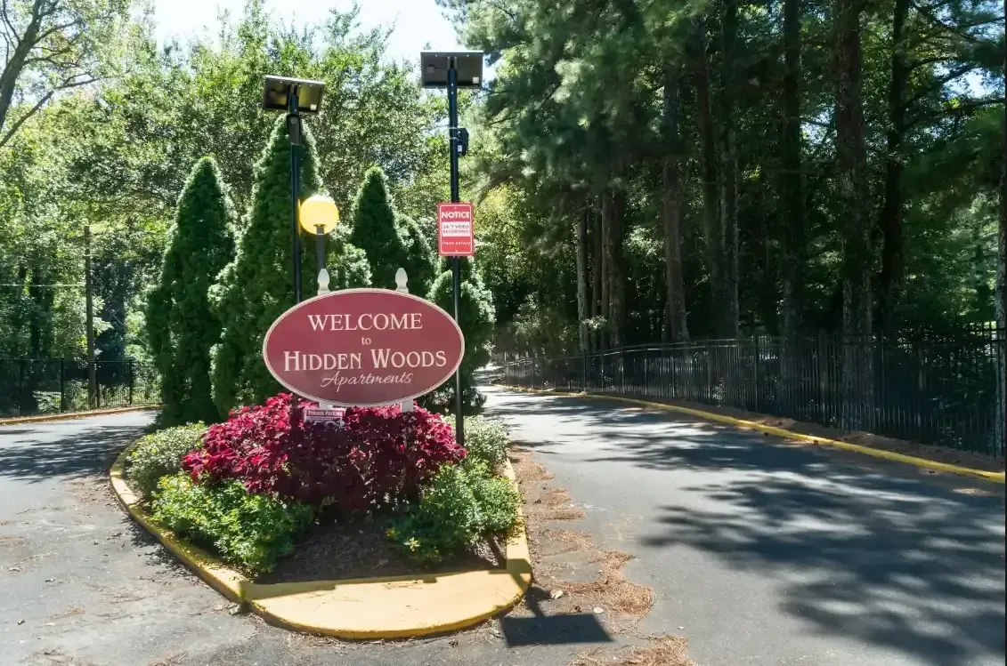Entrance sign for Whispering Pine Woods amid flowers and trees along a paved road