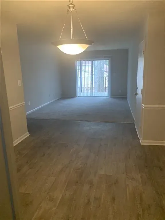 Empty living and dining area with wood flooring, beige walls, and sliding glass doors at the far end