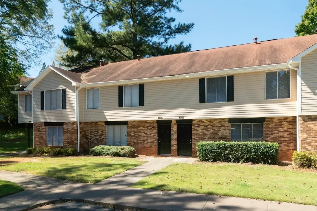 Two-story beige apartment building with brick lower level and grassy lawn in front