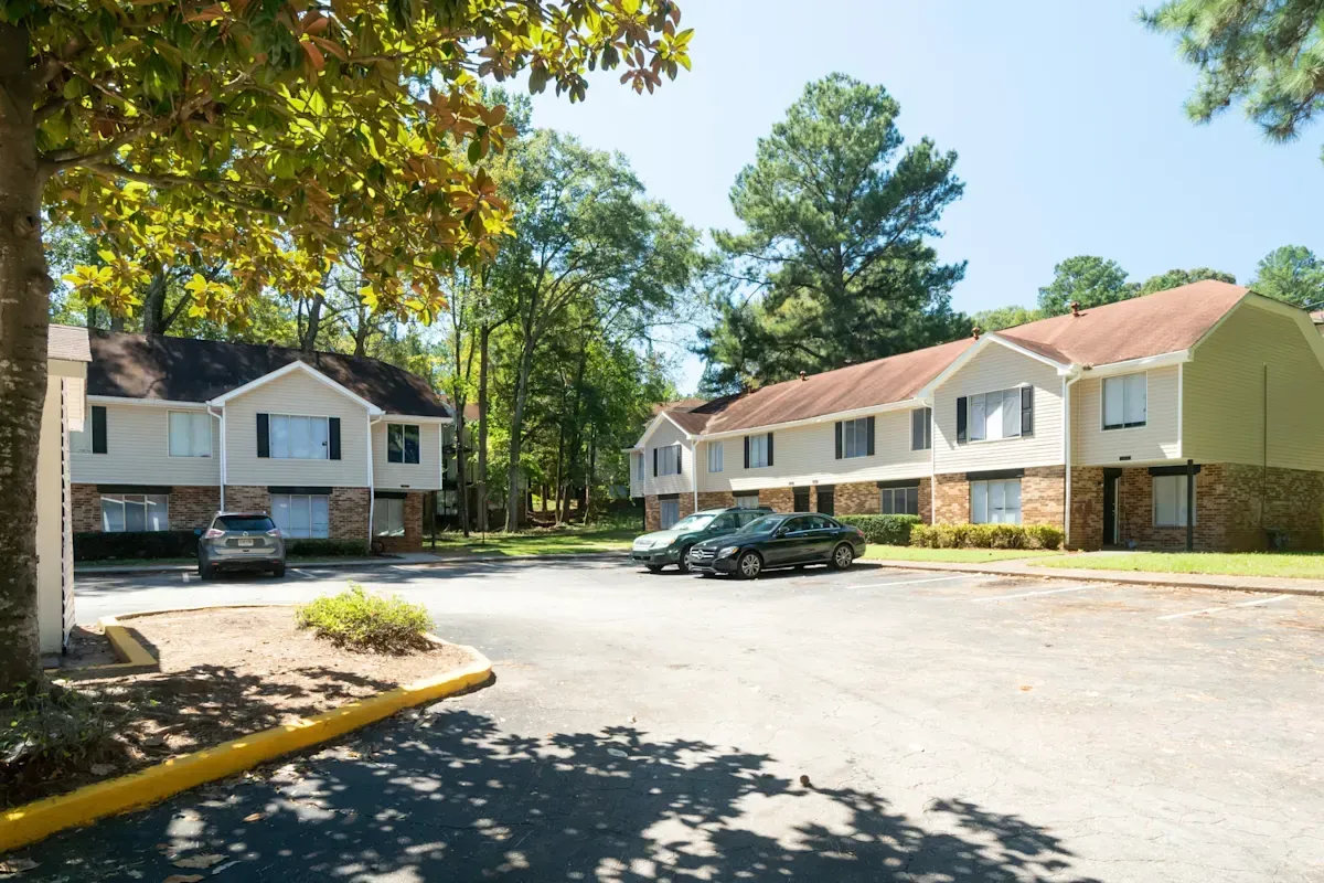Apartment complex parking lot with two-story beige buildings and parked cars under trees