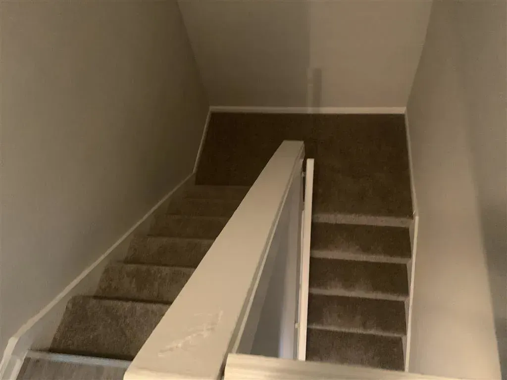 Carpeted staircase with central white banister in a beige hallway, viewed from the top landing
