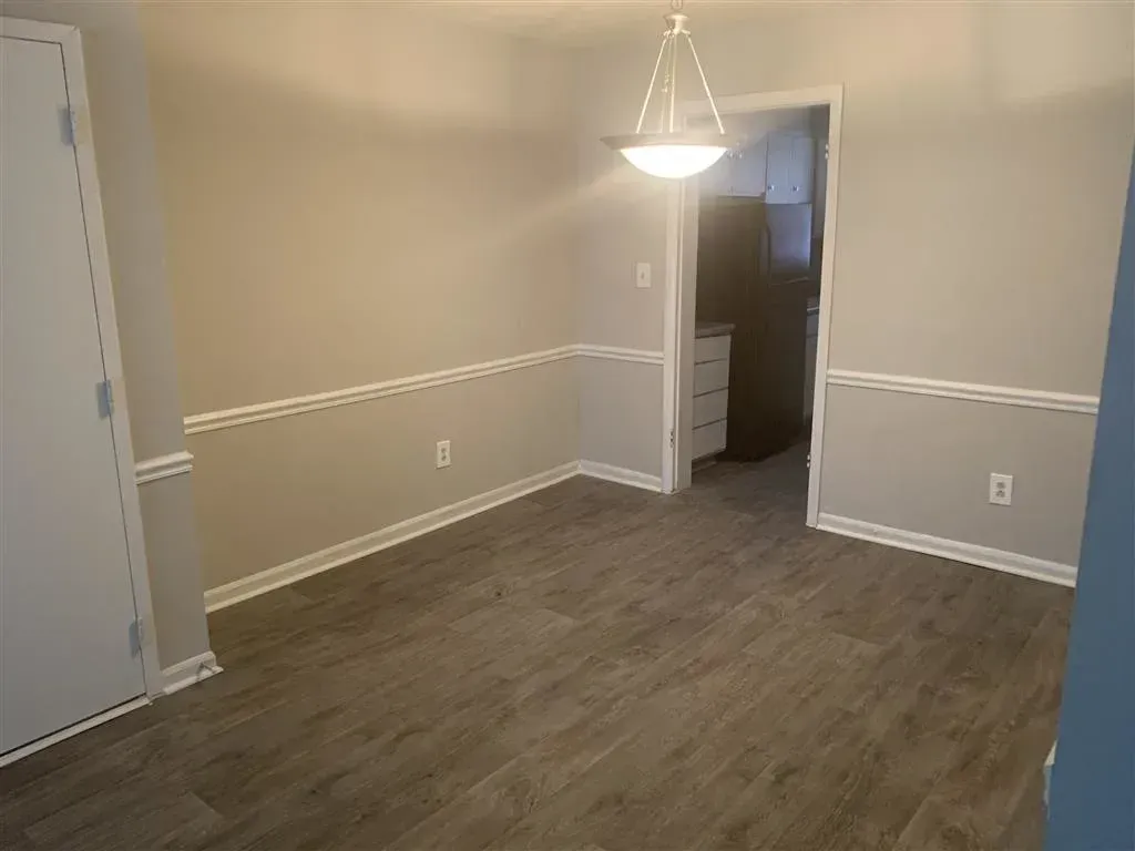 Empty beige dining room with gray wood flooring and a hanging light fixture, open doorway in back