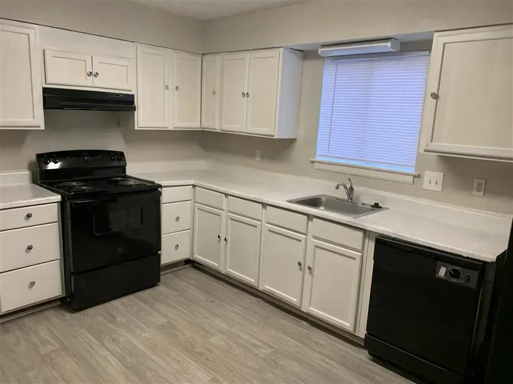 White kitchen with black appliances, white cabinets, and a window over the sink
