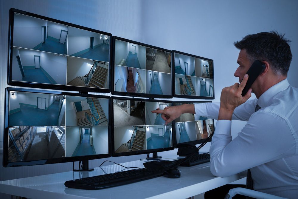 A Man Is Talking On A Cell Phone While Looking At A Bunch Of Monitors  — Surveillance NQ In Cairns, QLD
