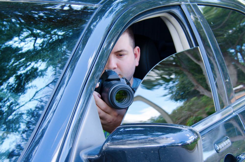 A Man Is Sitting In A Car Taking A Picture With A Camera — Surveillance NQ In Aitkenvale, QLD