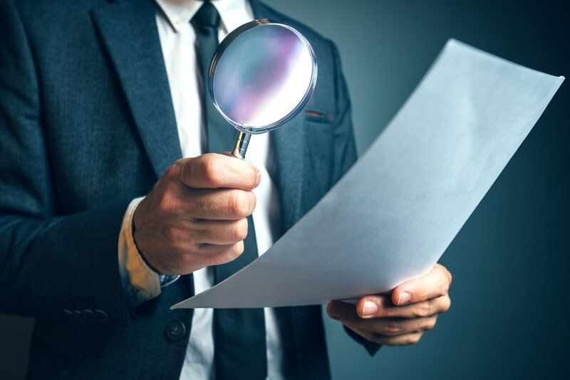 A Man In A Suit Is Holding A Magnifying Glass Over A Piece Of Paper  — Surveillance NQ In Cairns, QLD
