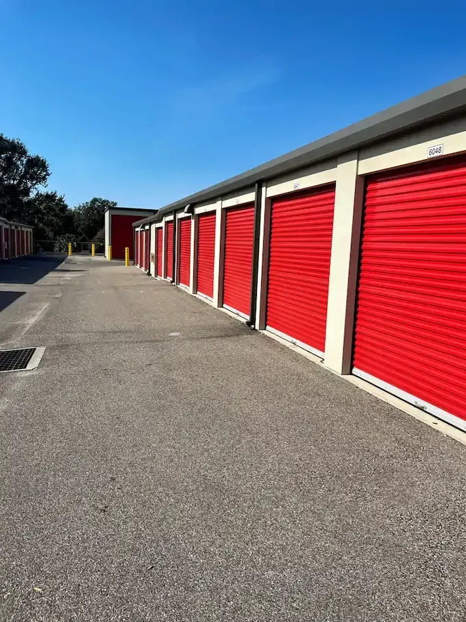 Red storage unit doors along a concrete path under a clear blue sky.