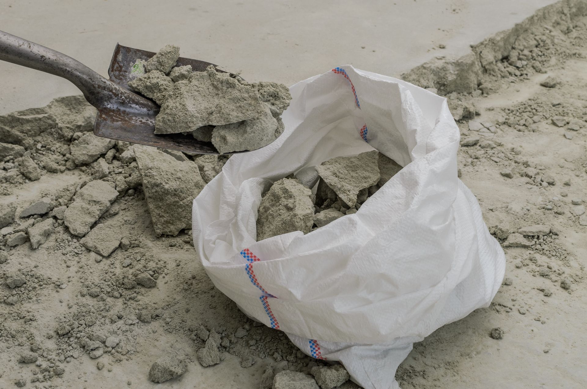 Shovel scooping debris into a white plastic bag on a concrete surface.