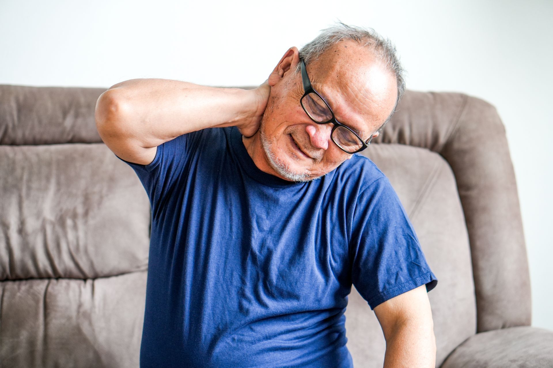 Man sitting on a couch, holding his neck with a pained expression