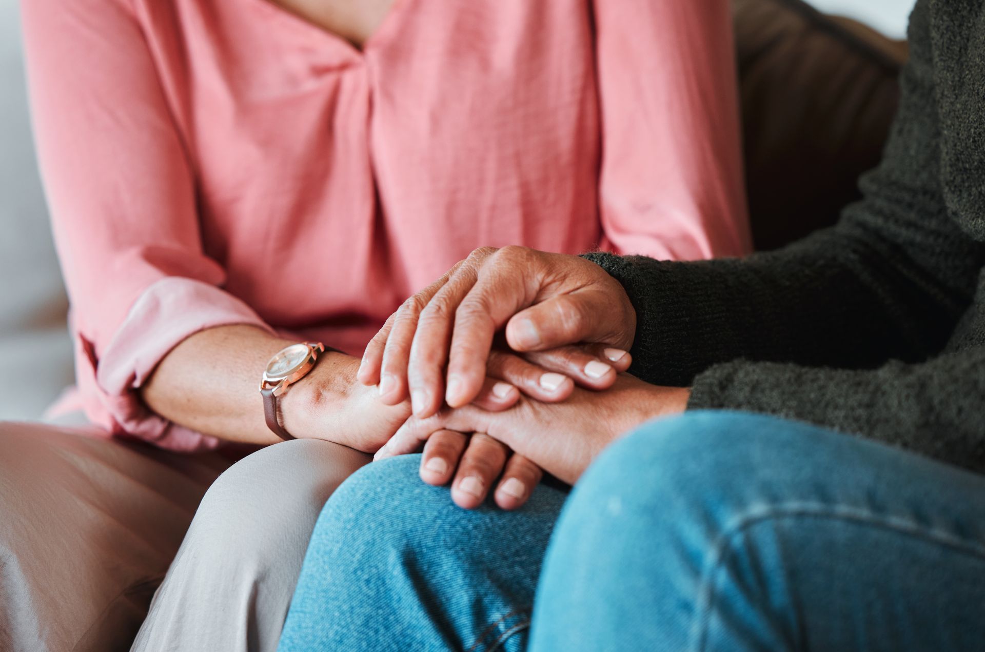 Two people sit close together, holding hands on a sofa, suggesting support and comfort.