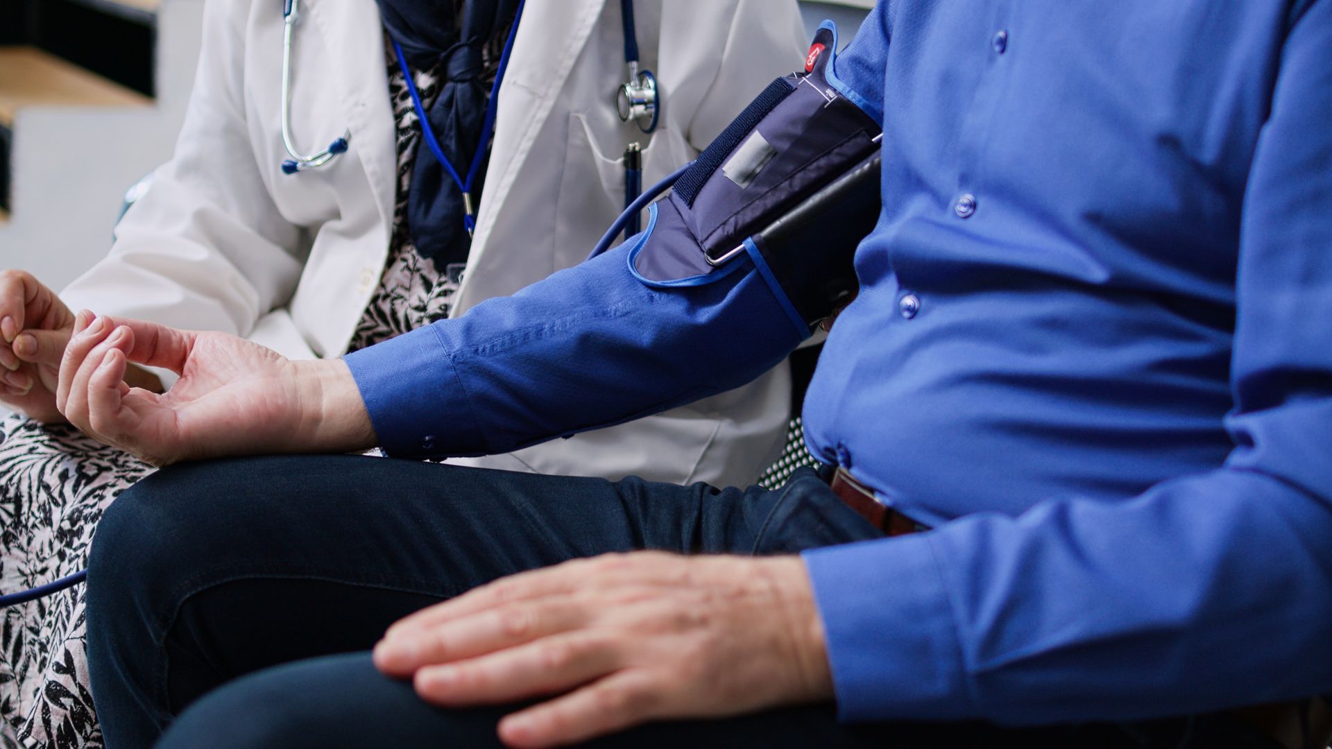 Doctor taking a blood pressure reading on a seated patient’s arm with a cuff.