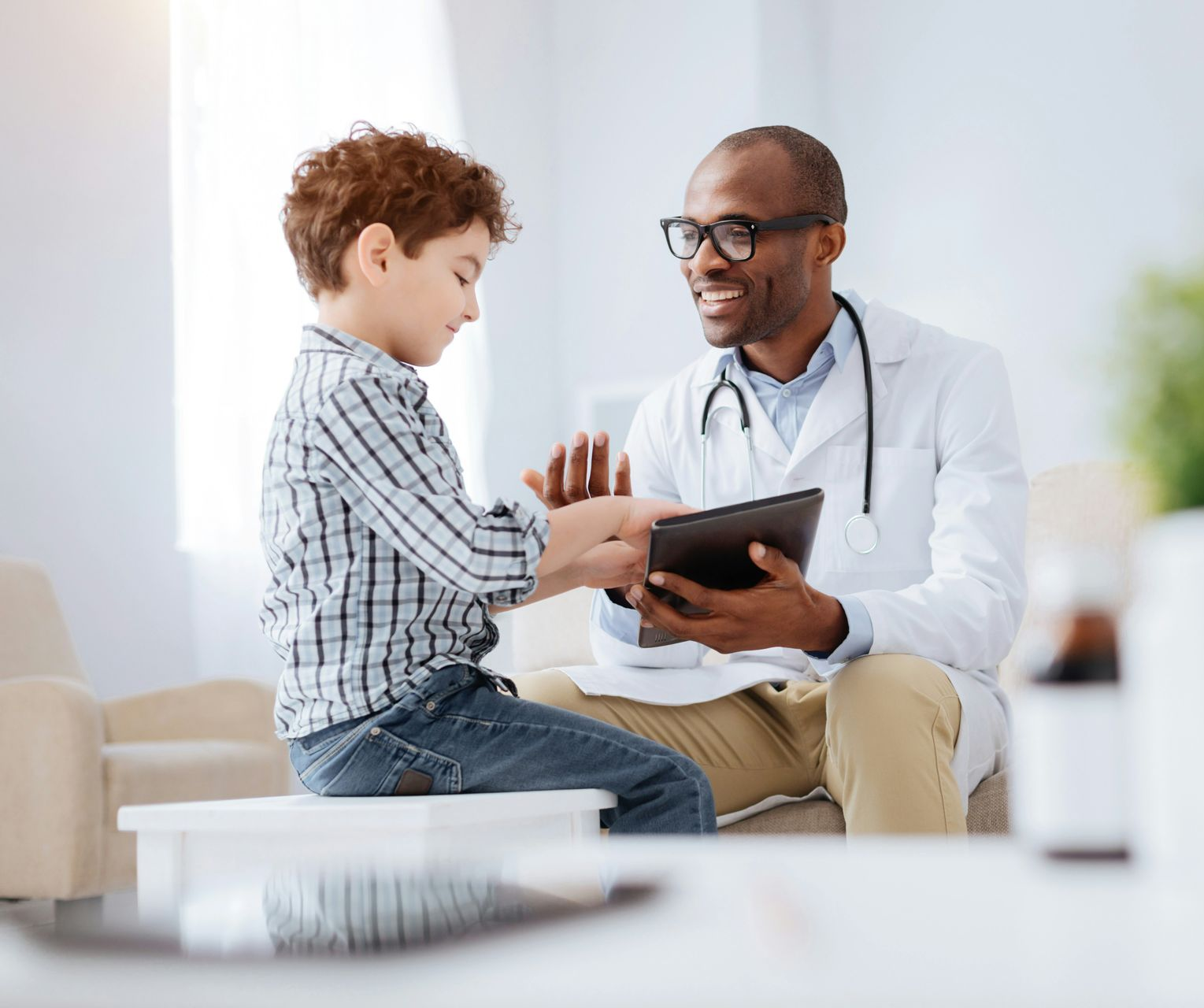 Doctor consulting a child with a tablet in a bright clinic, both smiling and engaged.